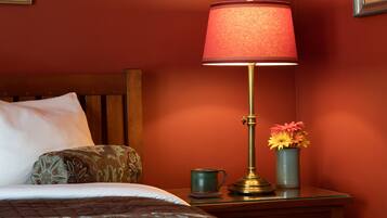 A neatly made bed with a patterned pillow, a bedside table with a lamp, a vase with flowers, and a mug.