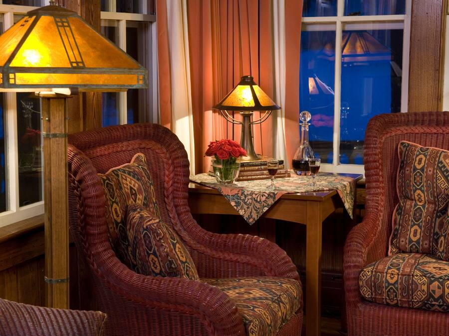 Une pièce chaleureuse avec des fauteuils en osier, une table ornée d’un vase de roses rouges et une lampe.