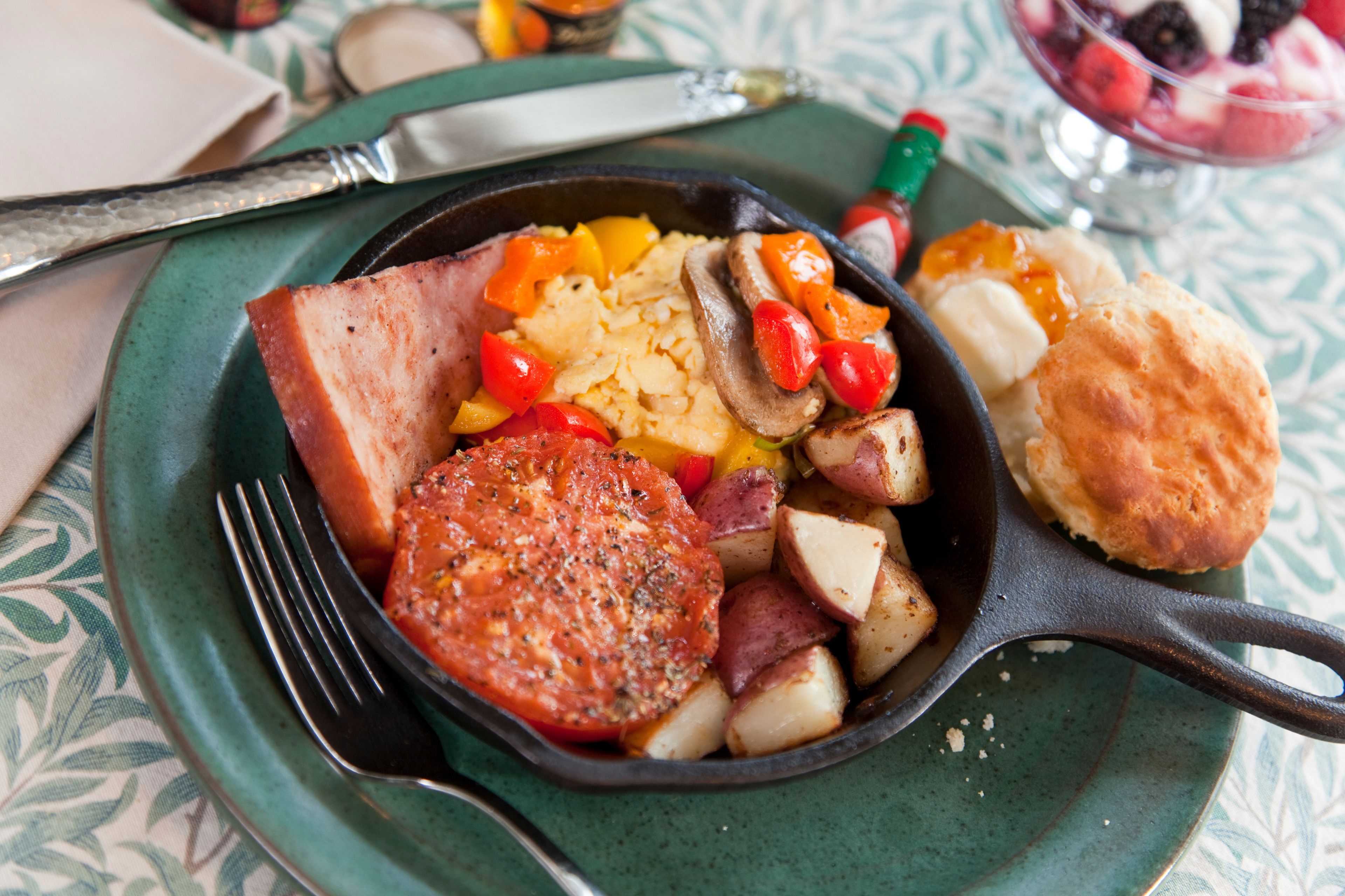 A skillet with breakfast items including eggs, potatoes, and sausage on a green plate.