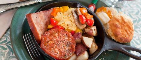 A skillet with breakfast items including eggs, potatoes, and sausage on a green plate.