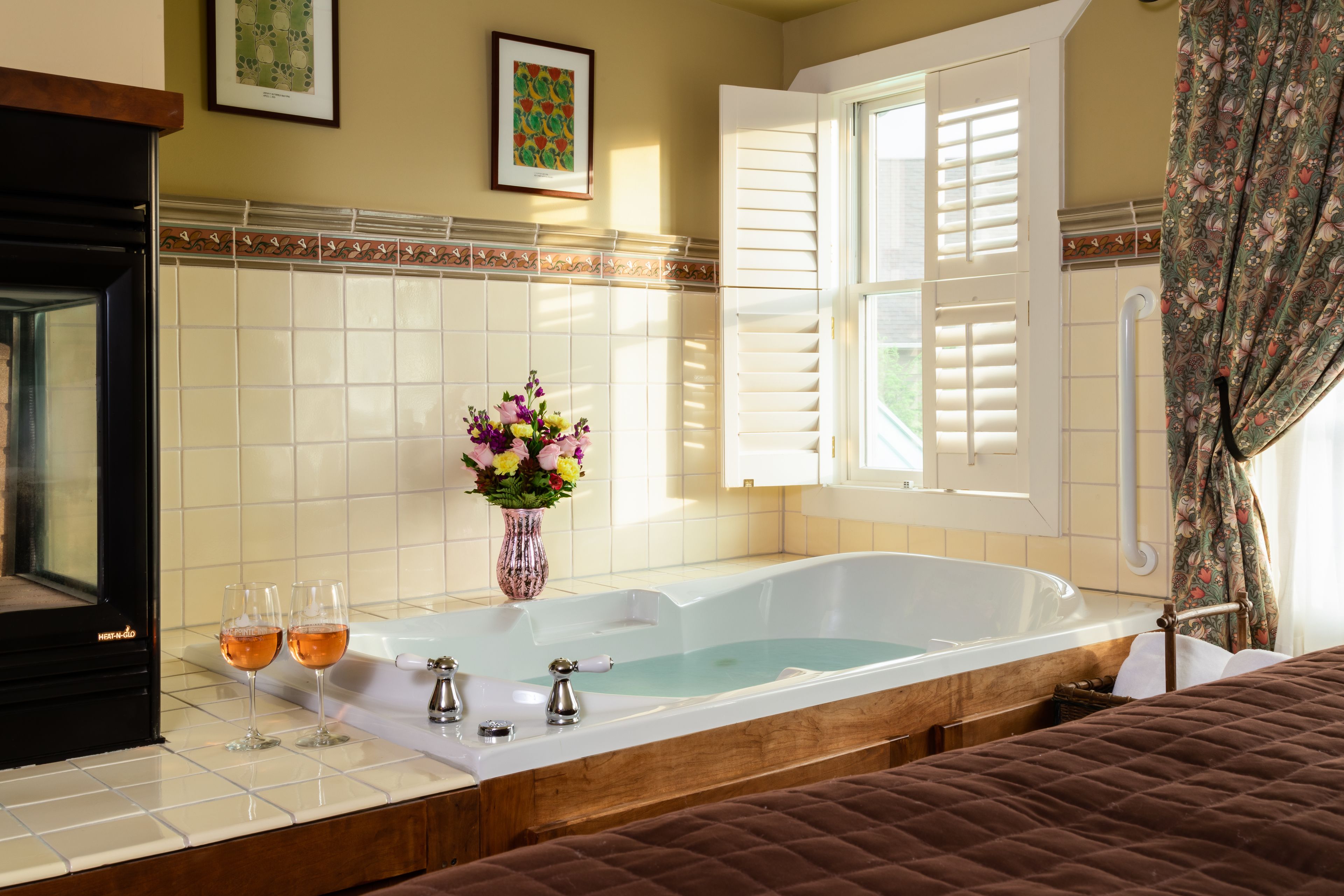 A bathroom with a bathtub, two glasses of wine, and a vase of flowers.