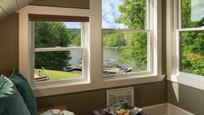 A room with a view of a lake, a sofa, a table with a tray of cookies, and a book. - Lake Pointe Inn (McHenry)