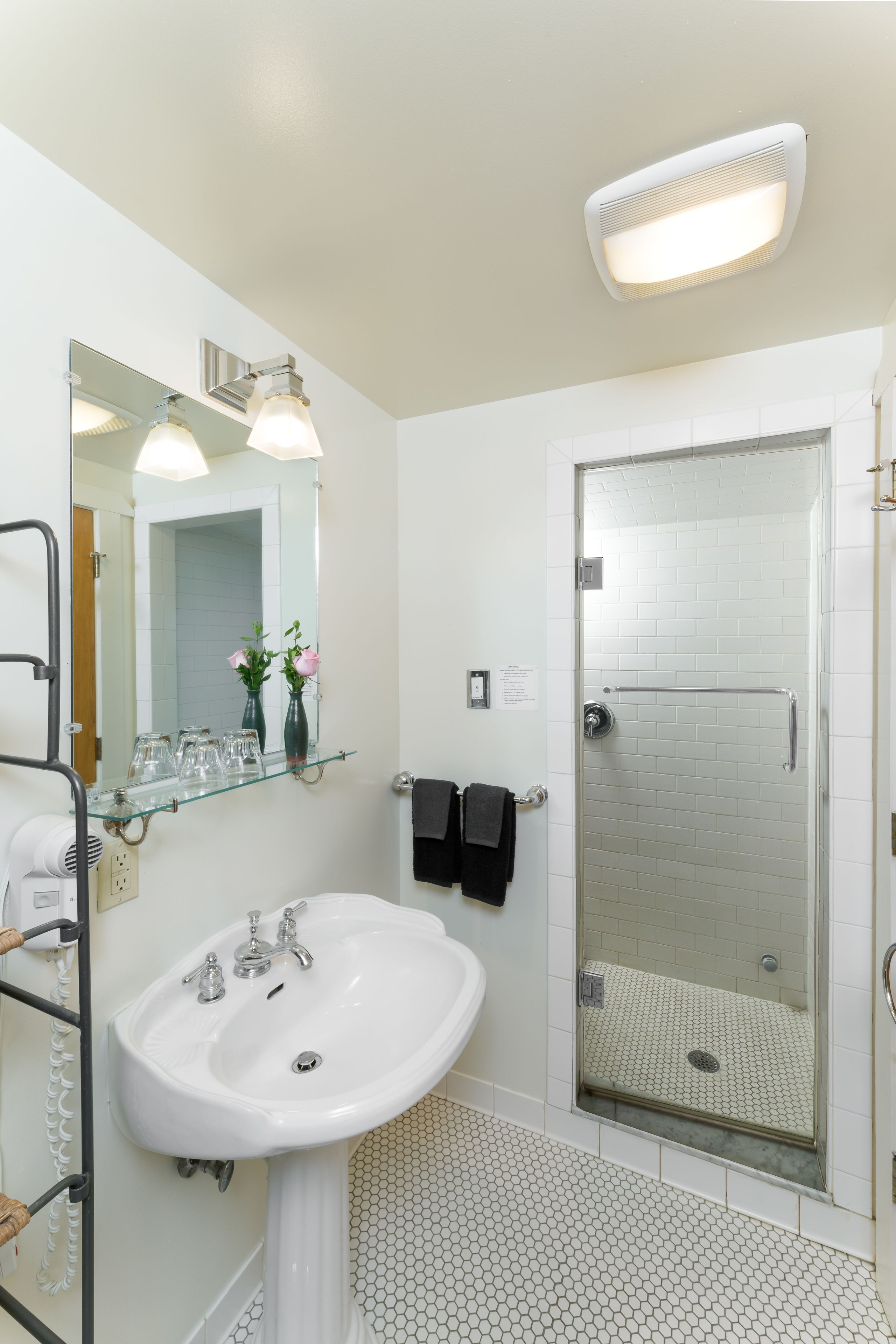 A bathroom with a white sink, a glass shower enclosure, and a mirror with a glass shelf above it.