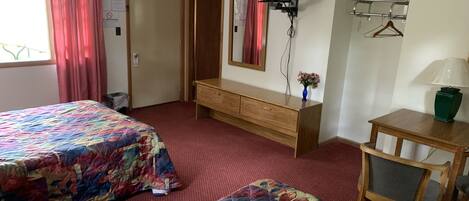 A hotel room with two beds, a wooden dresser, a television mounted on the wall, and a desk with a lamp.