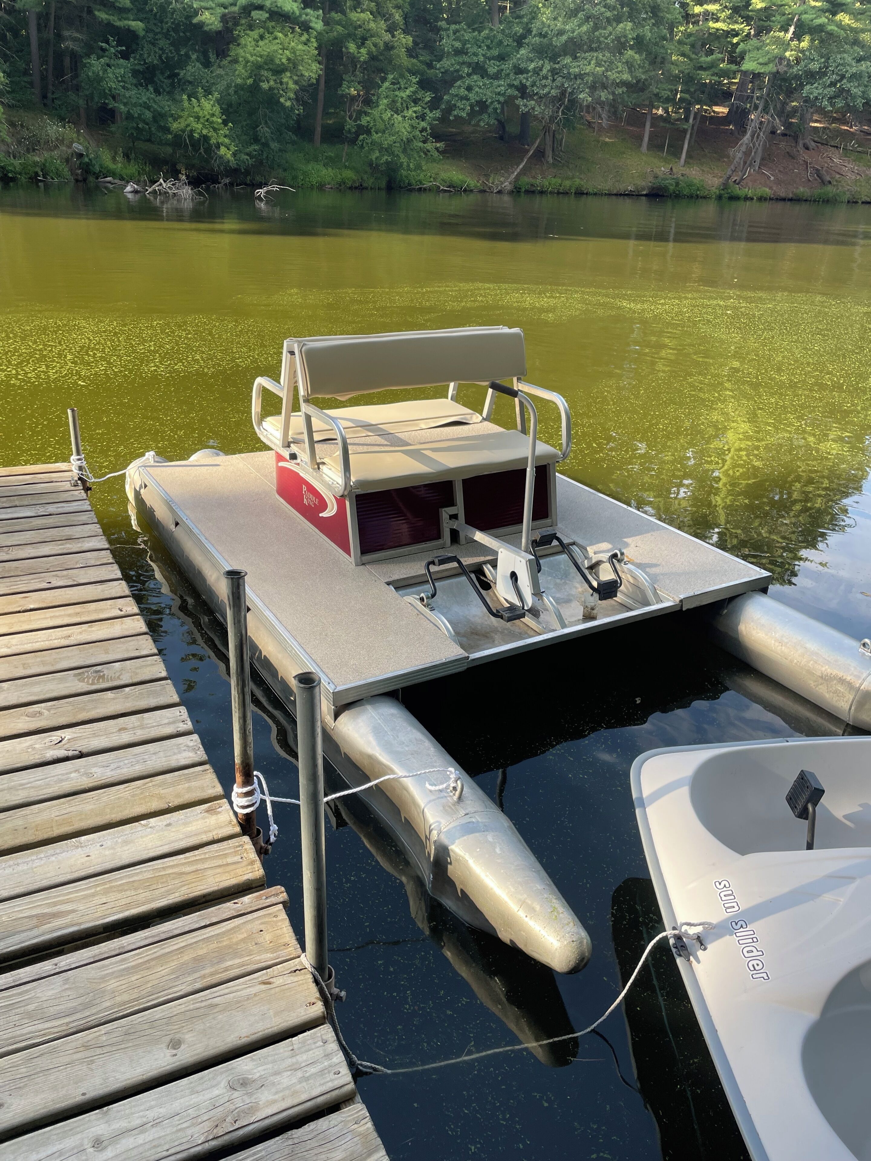 A docked boat with a bench and a small table, connected to a wooden dock.