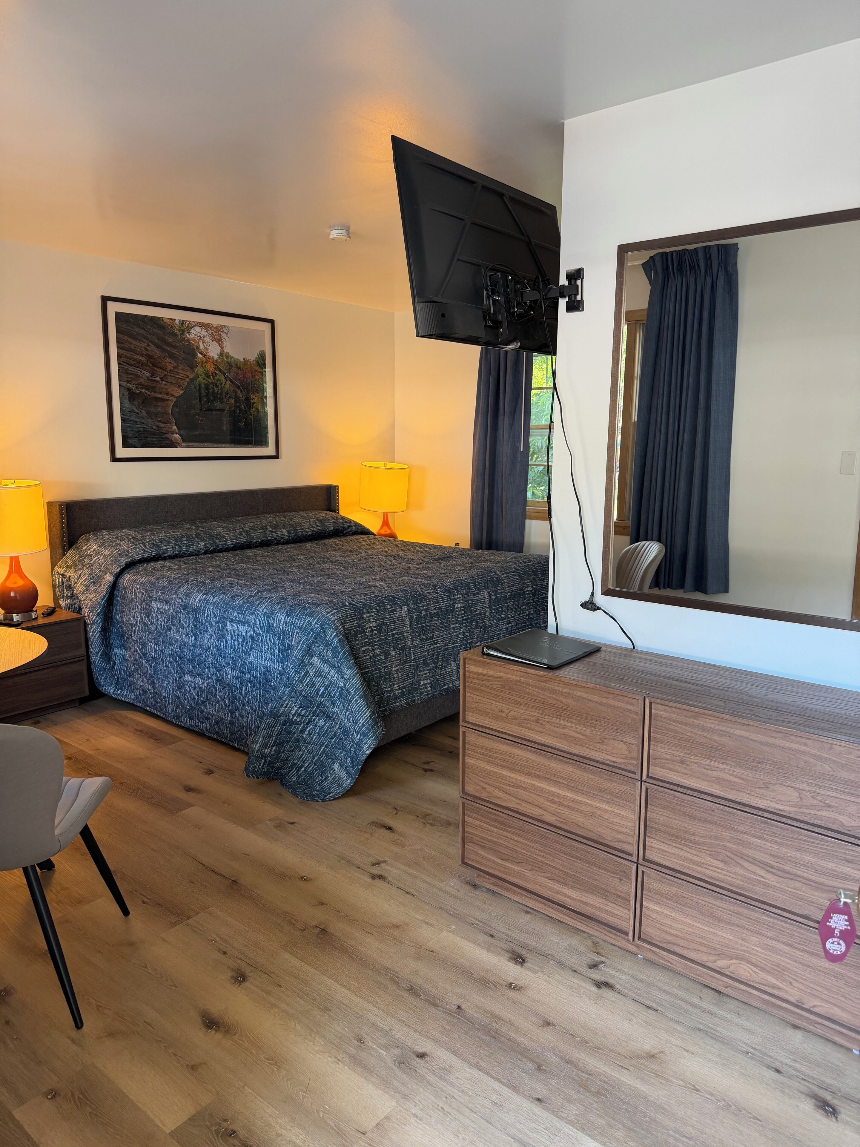 A bedroom with a bed, bedside lamps, a dresser, a television mounted on the wall, and a framed picture on the wall.