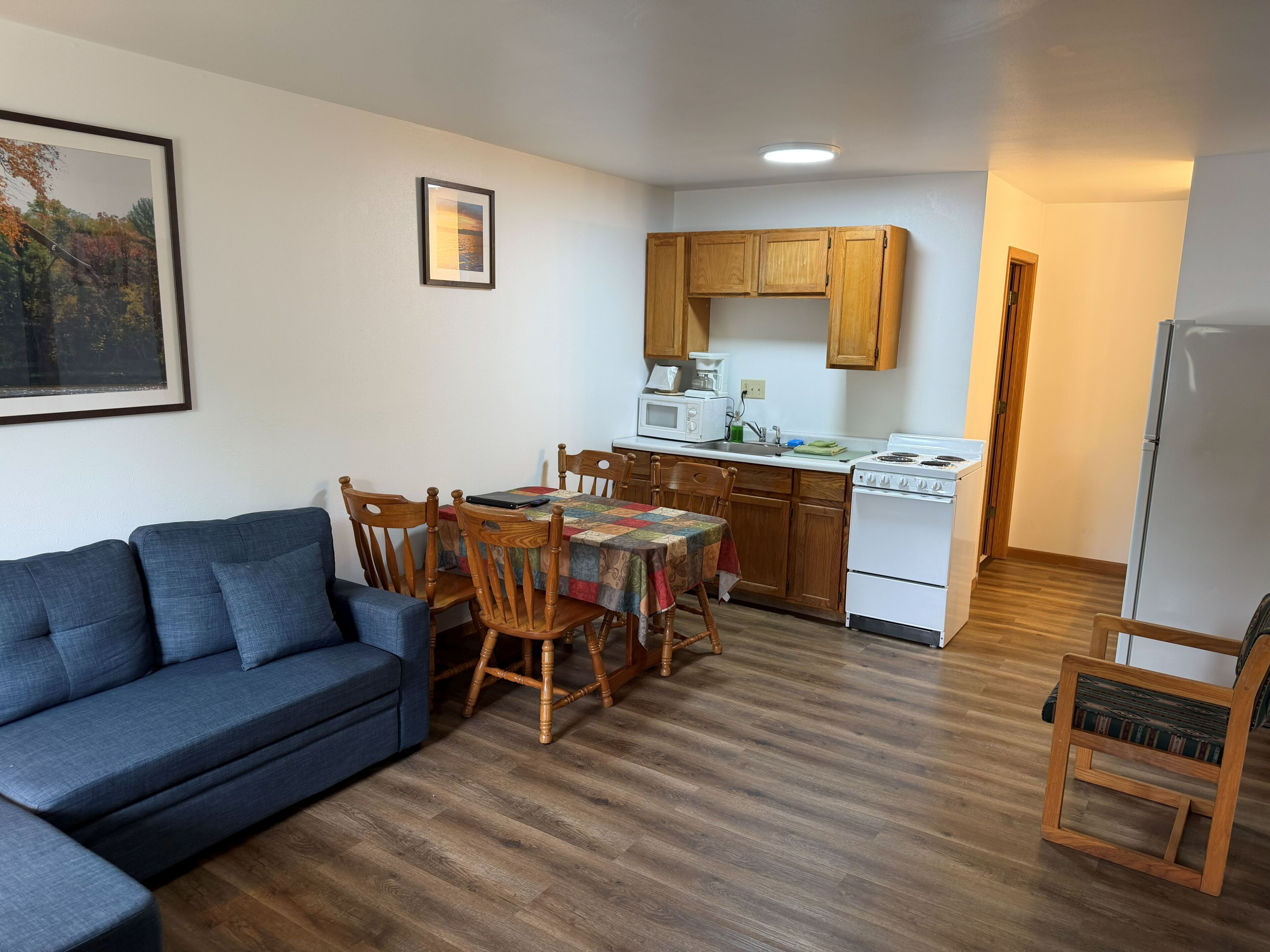 Un espacio habitable compacto con sofá, mesa de comedor, sillas, zona de cocina con armarios de madera, estufa y refrigerador.