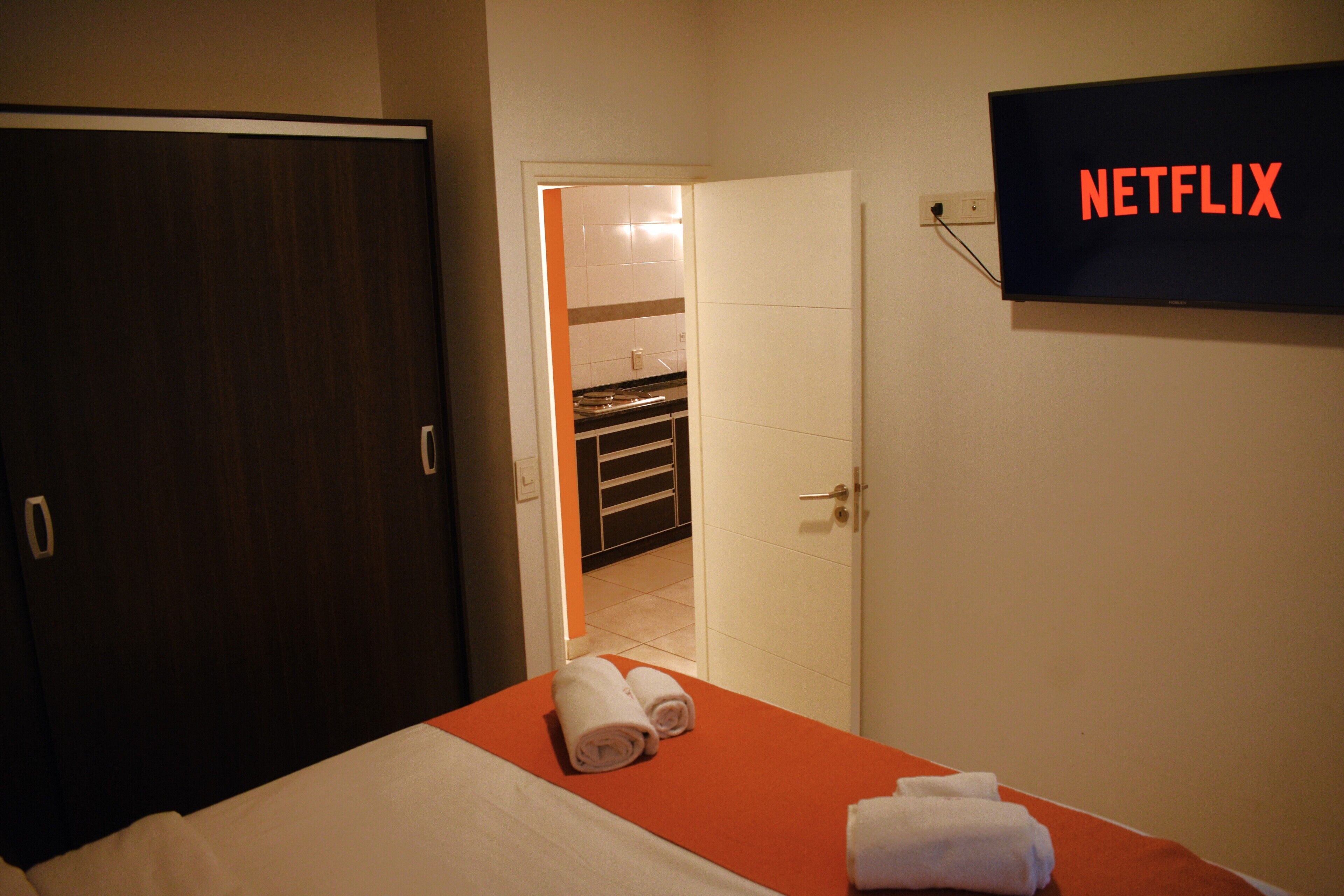 Une chambre d’hôtel avec un lit, un téléviseur affichant le logo « NETFLIX », et une salle de bain visible à travers une porte ouverte.