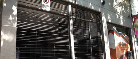 A building with closed metal shutters, a no parking sign, and a partial view of a colorful advertisement.