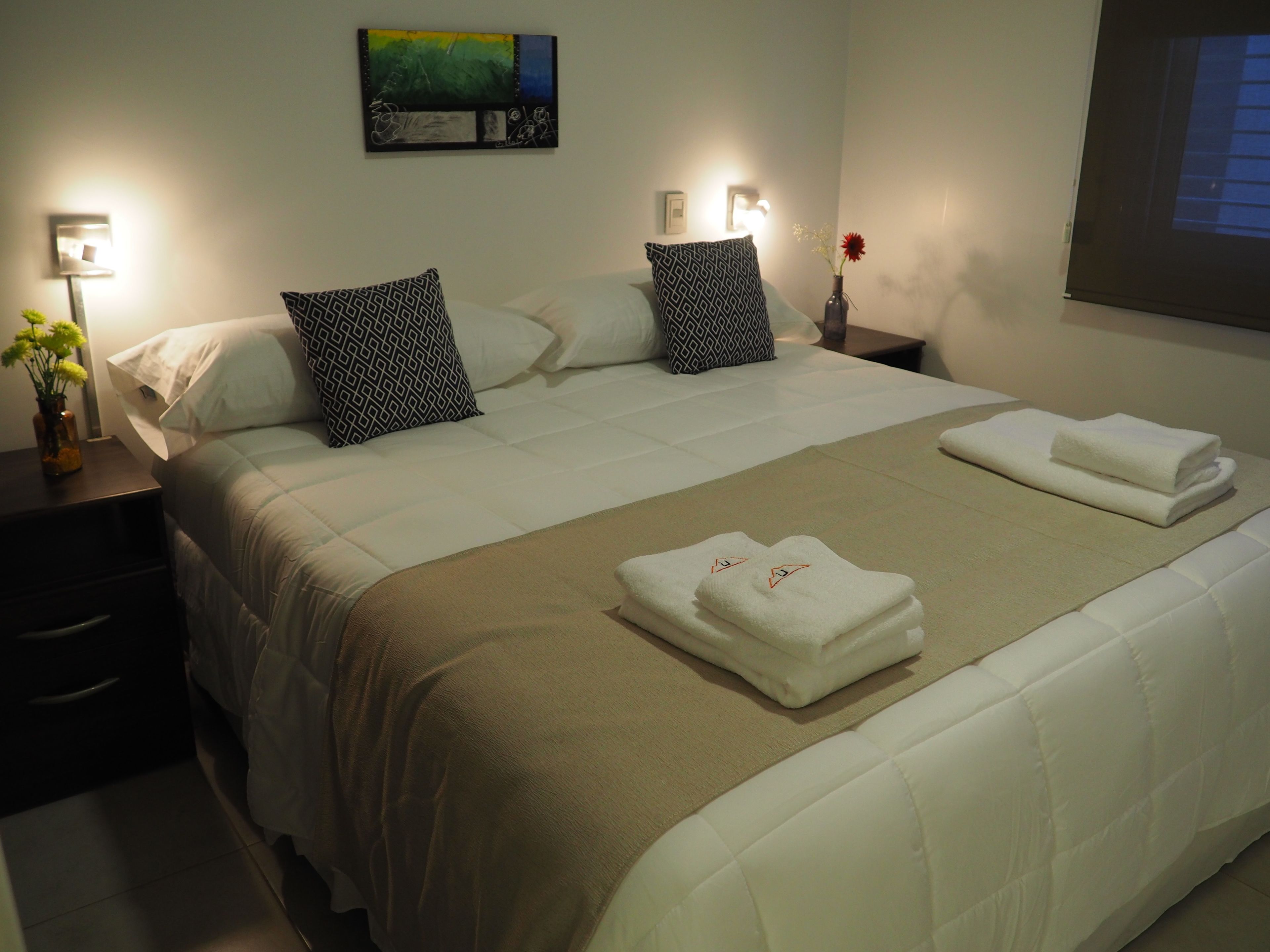 A neatly made bed with patterned pillows, a vase with flowers, and folded towels on the bed.