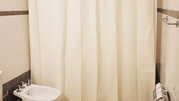 A bathroom with a shower curtain, a bidet, and a toilet.