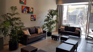 A modern living room with a brown leather sofa, two black ottomans, a large potted plant, and abstract wall art. - Umbral del Aconcagua (Mendoza)