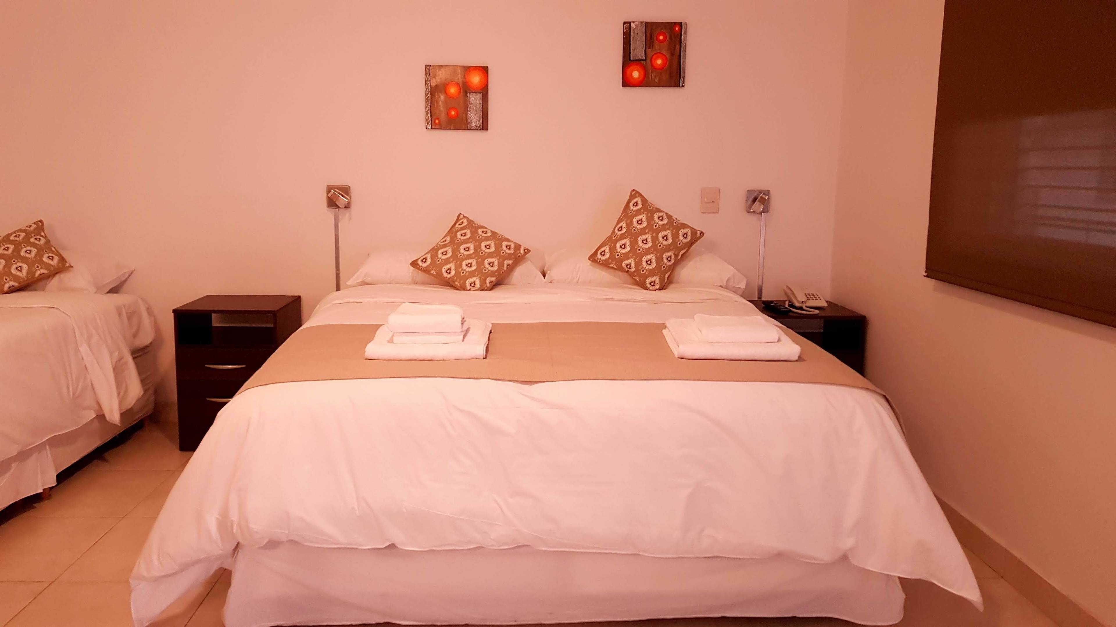 A hotel room with a large bed, two bedside tables, a nightstand, and two wall-mounted light fixtures.