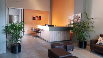 A modern reception area with a wooden counter, black leather chairs, and potted plants.