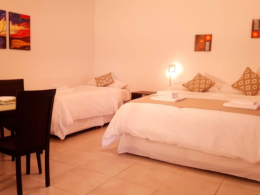 A hotel room with two beds, a dining table, chairs, and artwork on the walls.