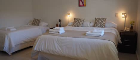Une chambre d’hôtel avec deux lits, chacun agrémenté de draps et d’oreillers blancs, une table de chevet avec une lampe et des œuvres d’art accrochées au mur.