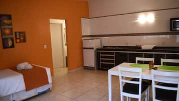 Una habitación de hotel compacta con una cama, una kitchenette pequeña y un comedor con sillas y una mesa.
