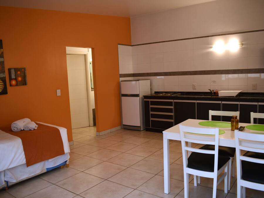 Una habitación de hotel compacta con una cama, una kitchenette pequeña y un comedor con sillas y una mesa.