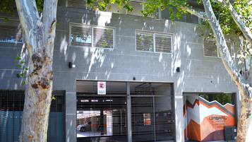 A modern building with a garage entrance, a no parking sign, and a large advertisement for 'UMBRAL DEL ACUDOR Apart Hotel'.