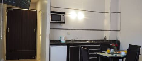 A compact kitchen with a microwave, a coffee maker, and a sink. There is a dining table with chairs and a small refrigerator.