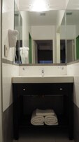 Une salle de bain avec un lavabo blanc, un miroir, un sèche-cheveux et un porte-serviettes.