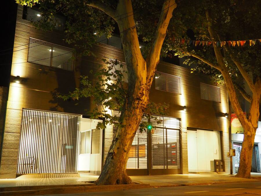 A building with a gated entrance, multiple floors, and a tree in front.