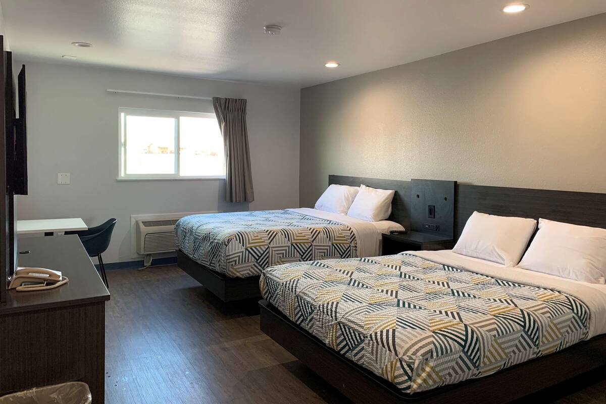 A hotel room with two beds, a desk with a telephone, a window with curtains, and a ceiling with recessed lighting.