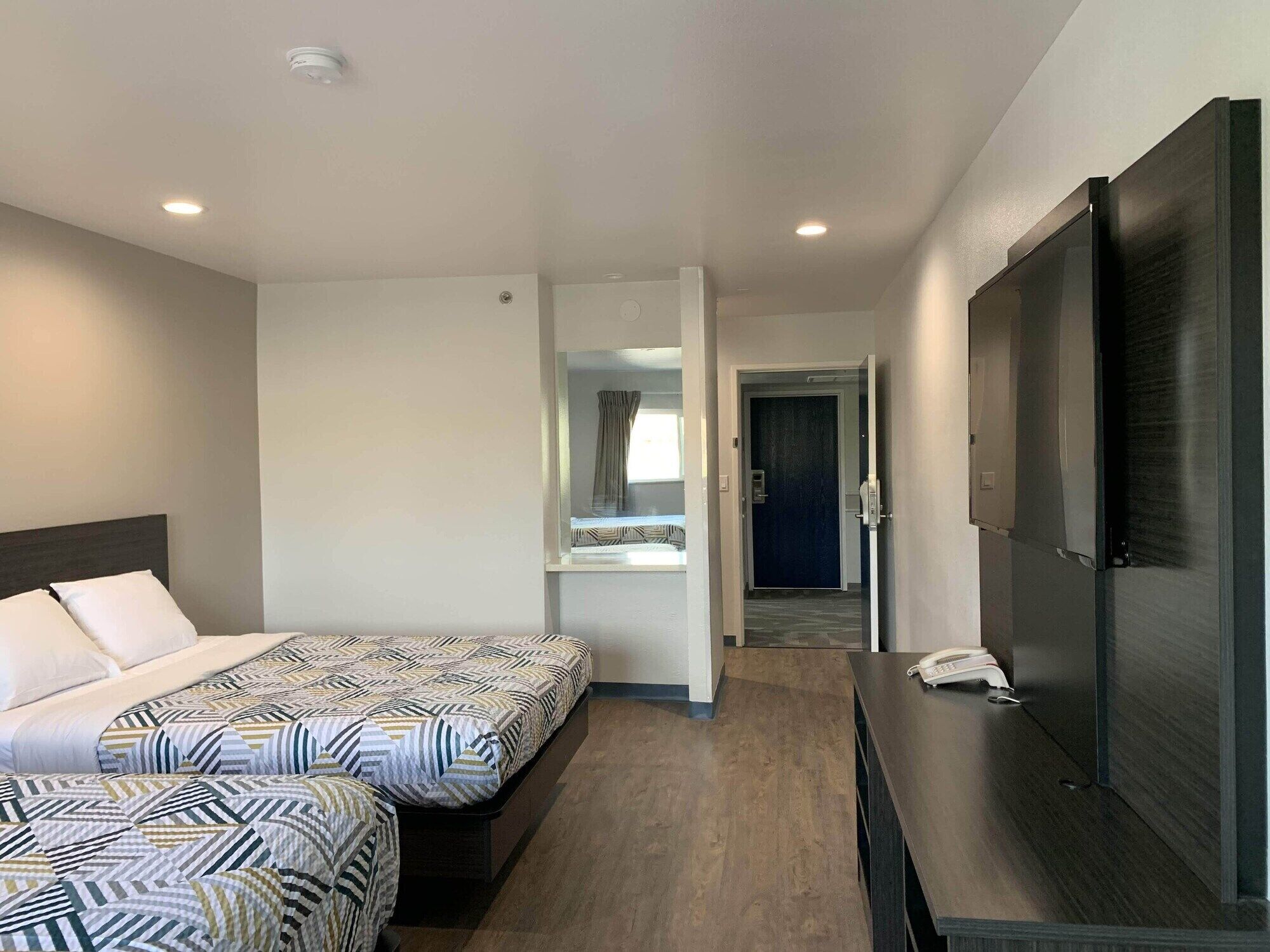 A hotel room with two beds, a large flat-screen TV, a desk with a phone, and a door leading to a hallway.