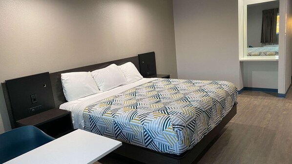 A neatly made bed with a patterned bedspread, a bedside table, and a chair. - Motel 6 Bullhead City, AZ (Bullhead City)
