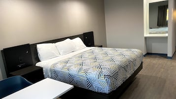 Habitación de hotel moderna con una cama grande, un escritorio pequeño y un ventanal con cortinas.
