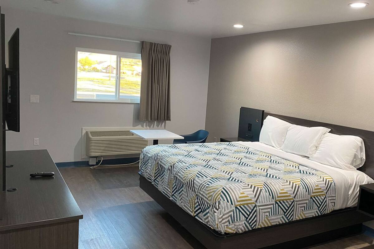 A modern hotel room with a large bed, a desk, and a TV.