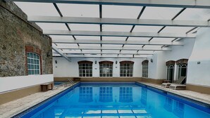 Una amplia piscina interior con agua azul cristalina, rodeada de paredes blancas y fachada de piedra.