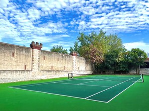 Cancha de tennis amb una xarxa, envoltada per una paret de pedra i arbres.