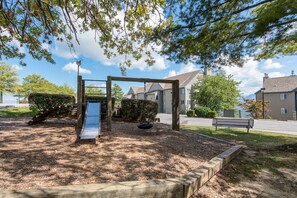 Relax on a bench near a play structure with a slide, surrounded by a gravel path and a low fence.