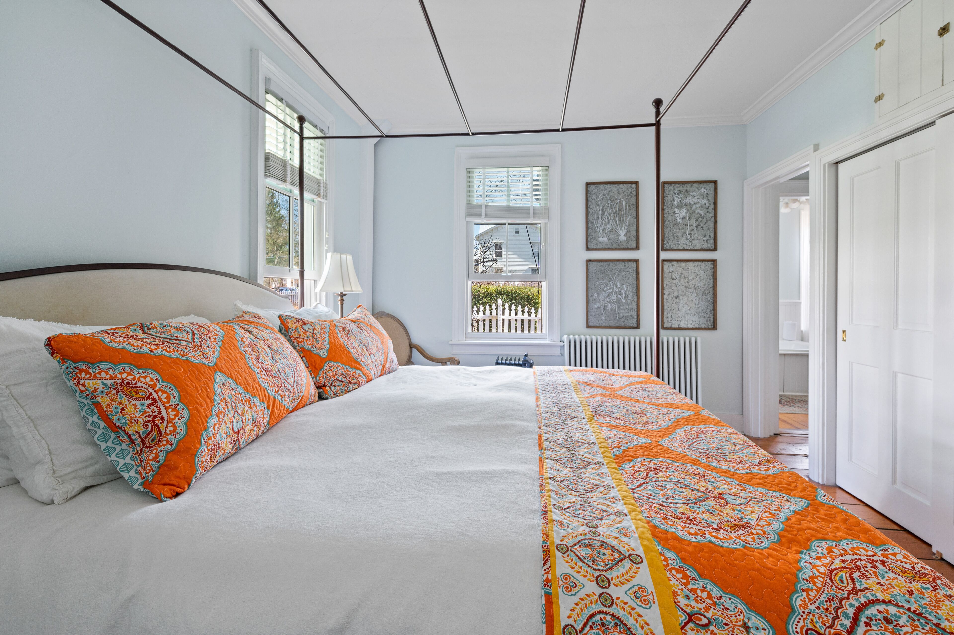 Een groot bed met wit en oranje beddengoed, een raam met uitzicht en een witte radiator.