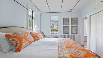 Een groot bed met wit en oranje beddengoed, een raam met uitzicht en een witte radiator.