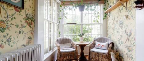 A cozy room with two wicker chairs, a radiator, and a window with a view of greenery.