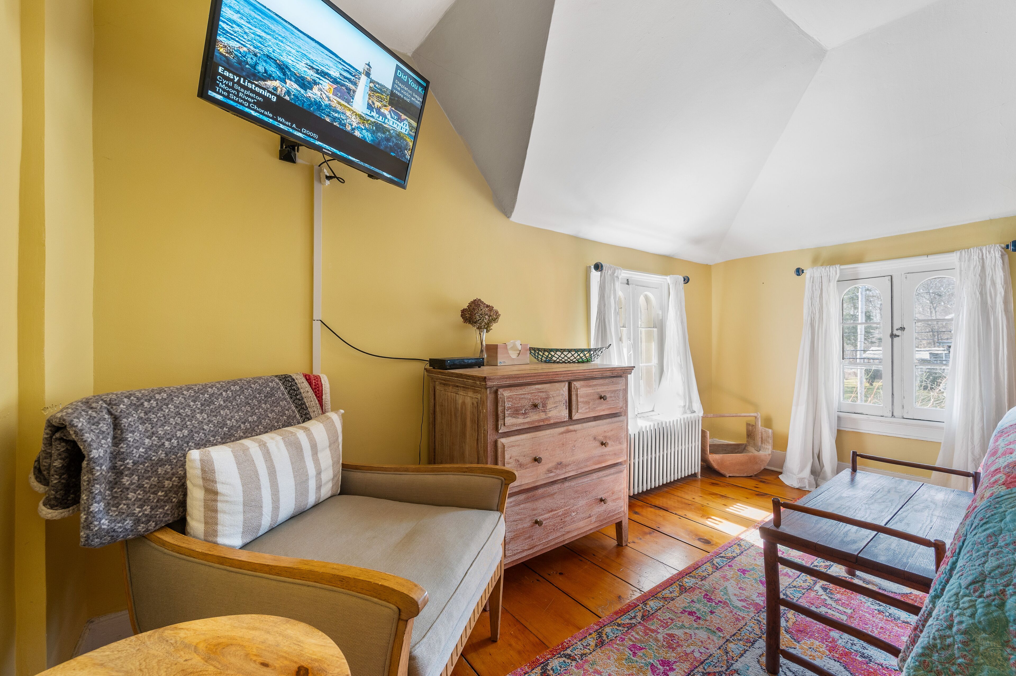 Ein gemütliches Zimmer mit einer Couch, einem Holzkleiderschrank, einem kleinen Tisch und einem an der Wand montierten Fernseher.
