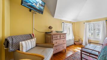 Ein gemütliches Zimmer mit einer Couch, einem Holzkleiderschrank, einem kleinen Tisch und einem an der Wand montierten Fernseher.
