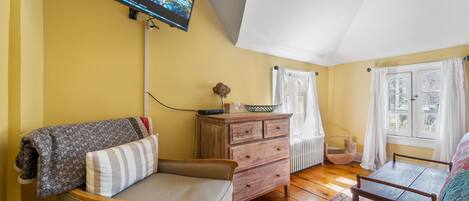 A cozy room with a sofa, a wooden dresser, a small table, and a TV mounted on the wall.