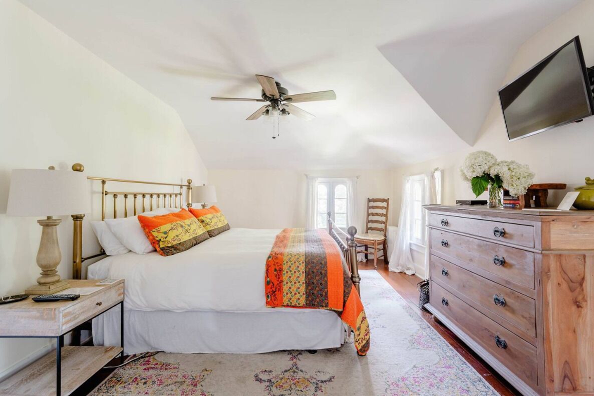 A bedroom with a bed, a nightstand, a dresser, a ceiling fan, a television, and a window.