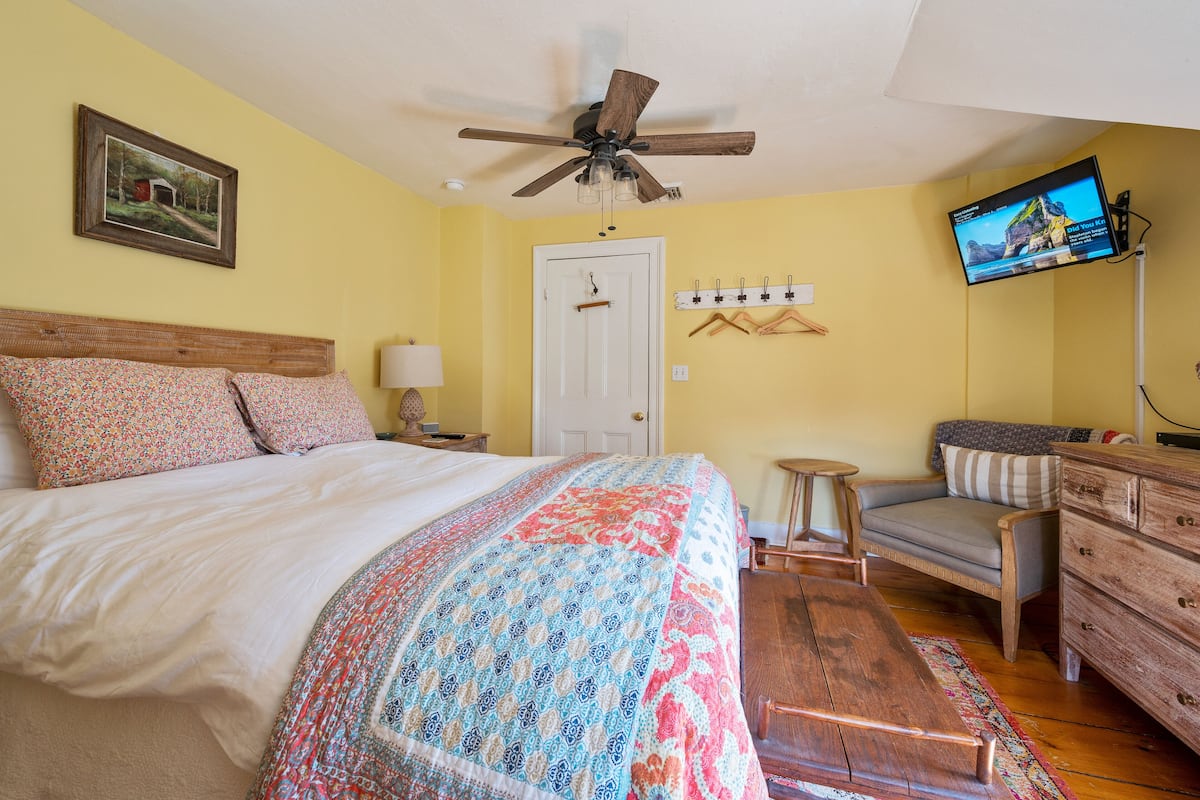 A bedroom with a bed, a ceiling fan, a TV, a dresser, and a chair.