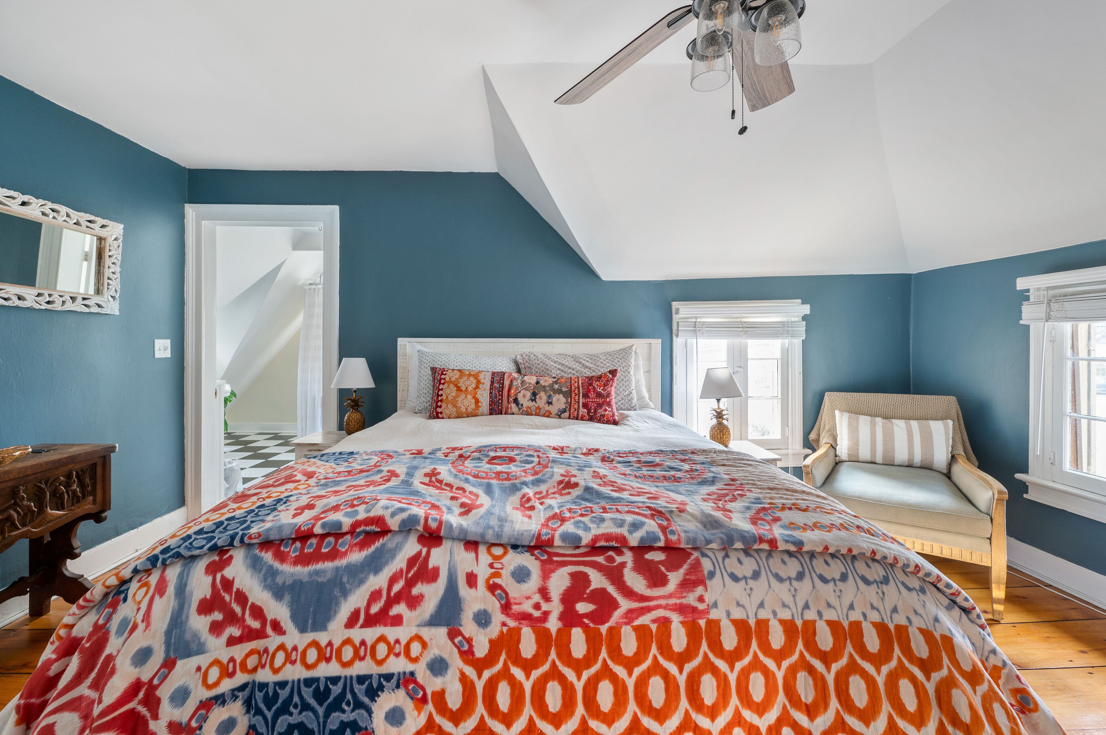 A bedroom with a large bed, a ceiling fan, and a view of a staircase.