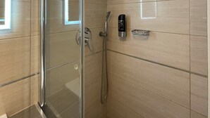 Un bagno moderno con box doccia in vetro, soffione a mano, pannello comandi a parete e specchio ad angolo.