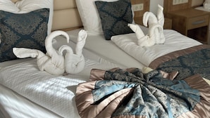 Una camera d'albergo con due letti, ognuno con cuscini bianchi e decorati, e una scultura di asciugamani sul letto.