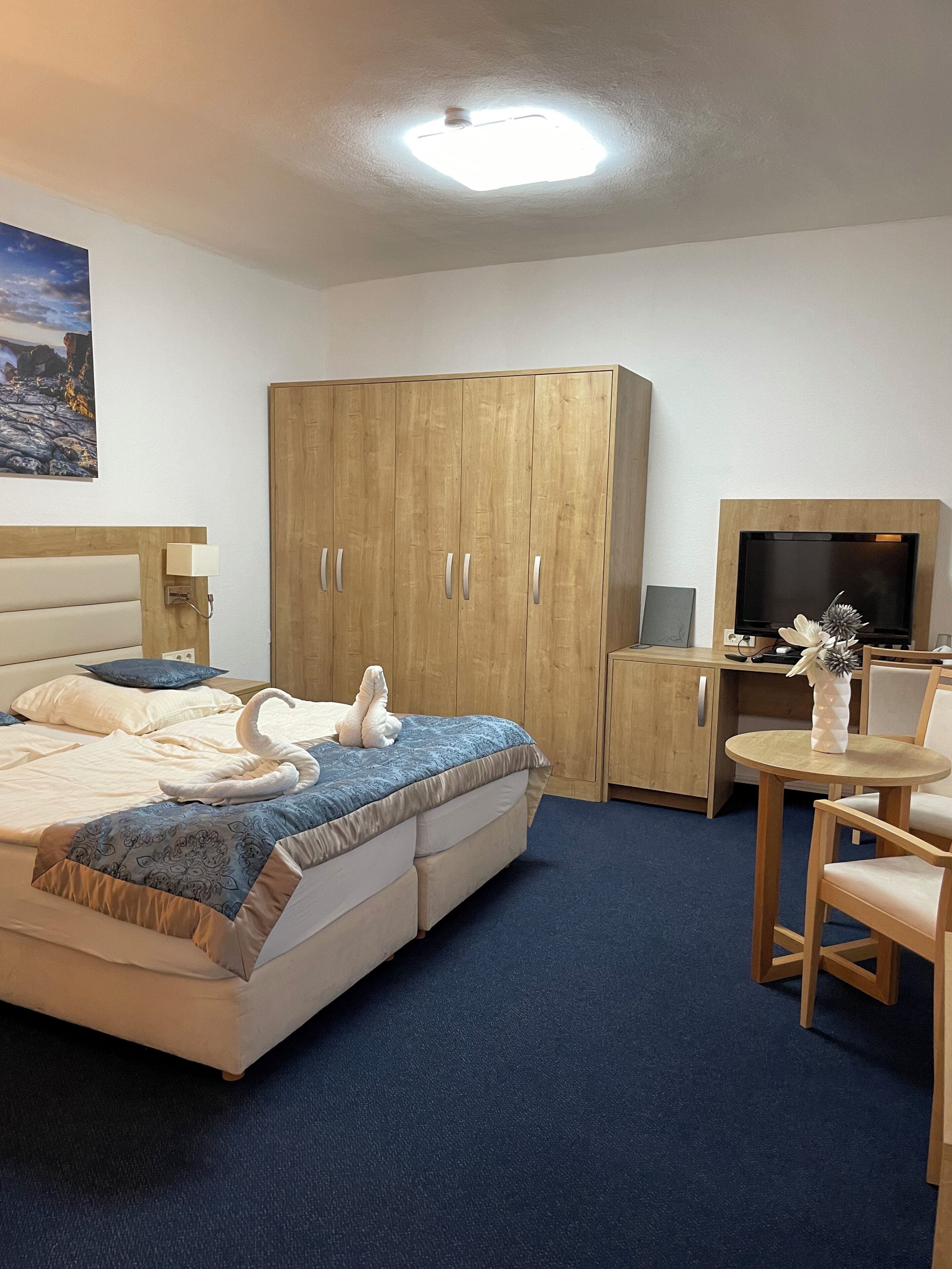 Ein Hotelzimmer mit einem Bett, einem Holzschrank, einem Schreibtisch mit Fernseher und einem kleinen runden Tisch mit Stuhl.