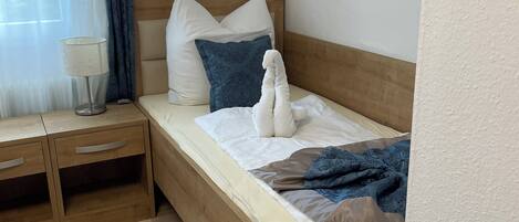 A neatly made bed with a wooden headboard, a bedside table with a lamp, and a blue patterned pillow.