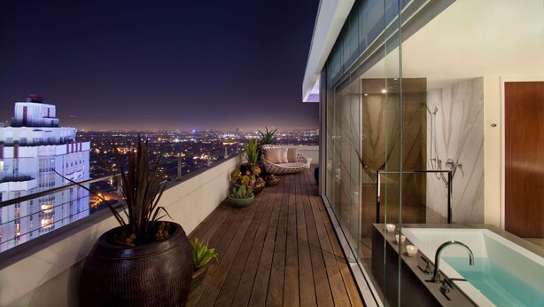 A balcony with a view of the city at night, a modern bathroom with a bathtub, and potted plants. - Andaz West Hollywood (West Hollywood)