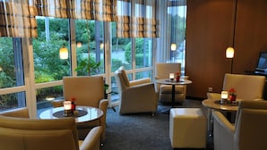 Habitación de hotel con zona de estar que incluye sillones y una pequeña mesa redonda, ventanas amplias con vista a zonas verdes y suelo alfombrado.