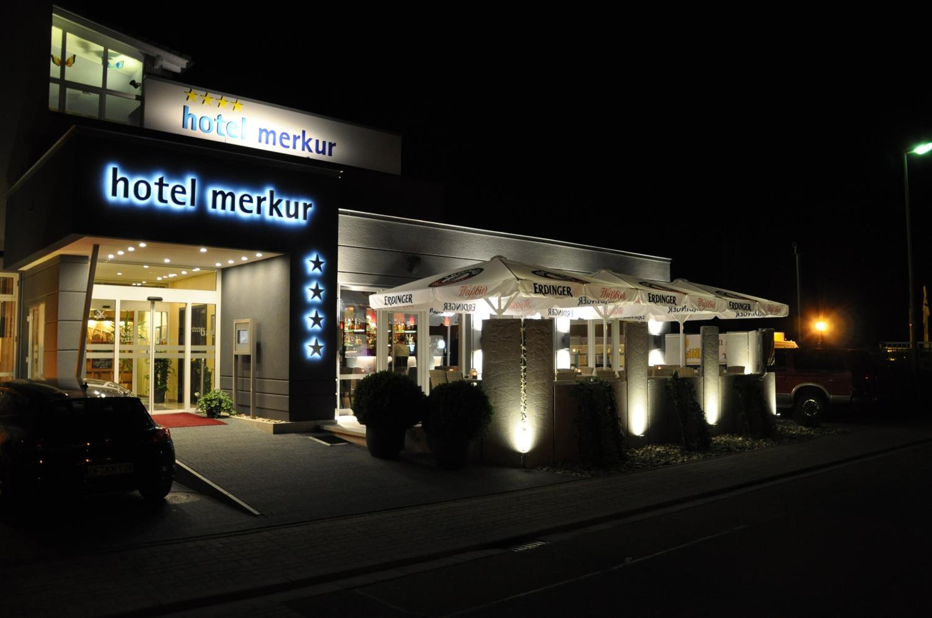 A hotel named 'hotel merkur' with a modern facade, outdoor seating area, and a visible entrance.